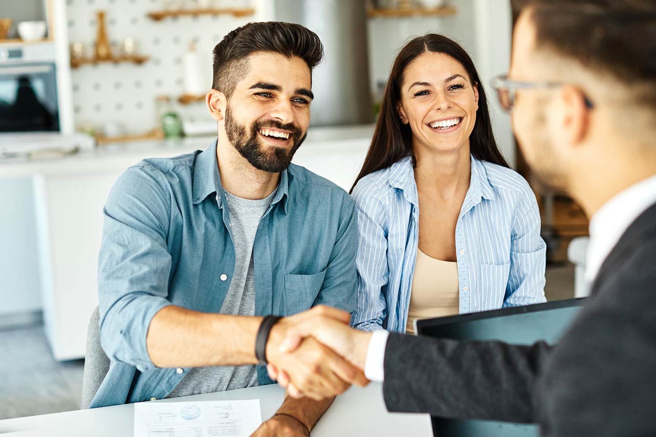 Real estate agent with couple shaking hands closing a deal and signing a contract